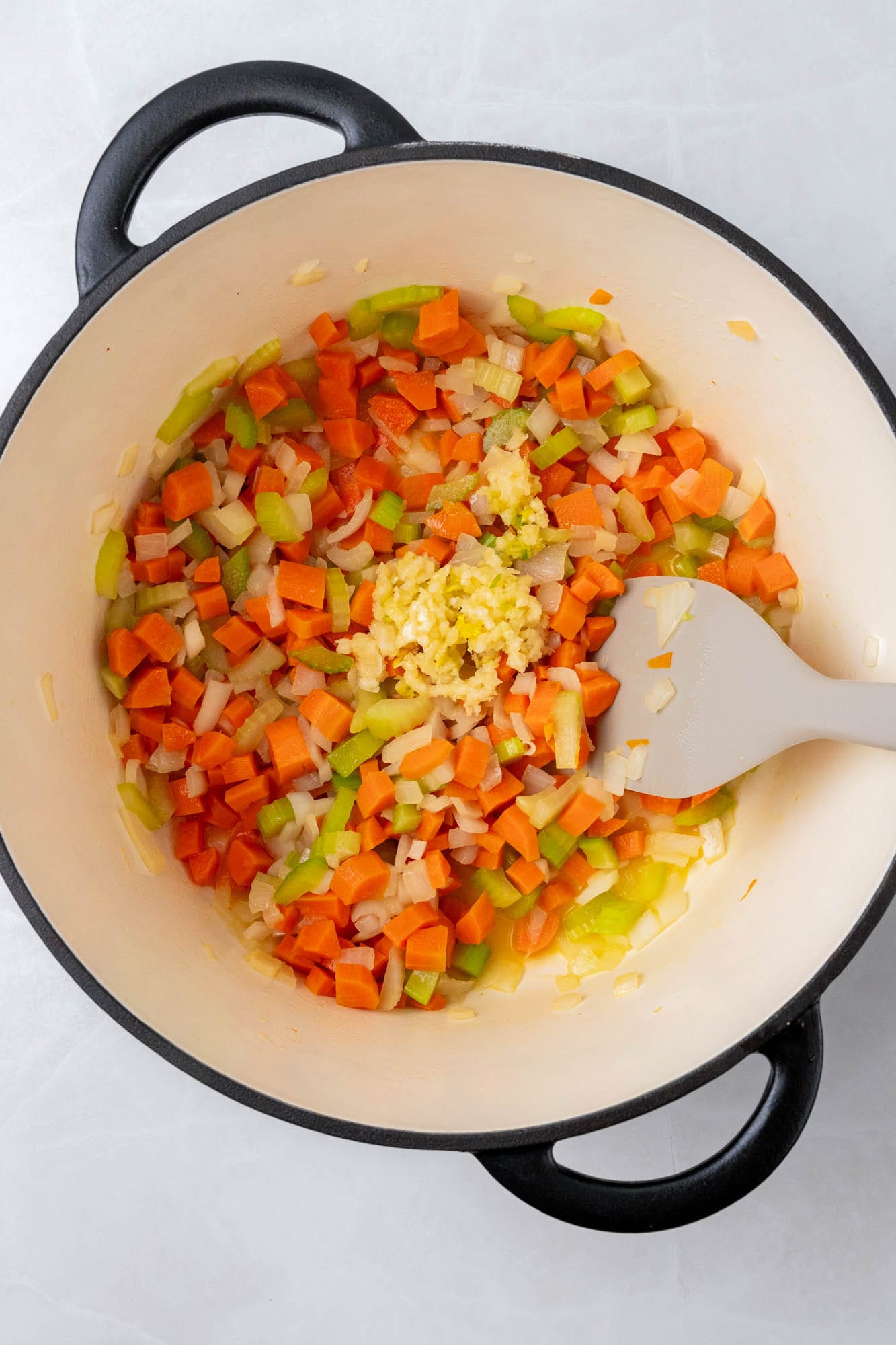 mirepoix in a dutch oven, sauteed with a gray spatula, minced garlic added in.