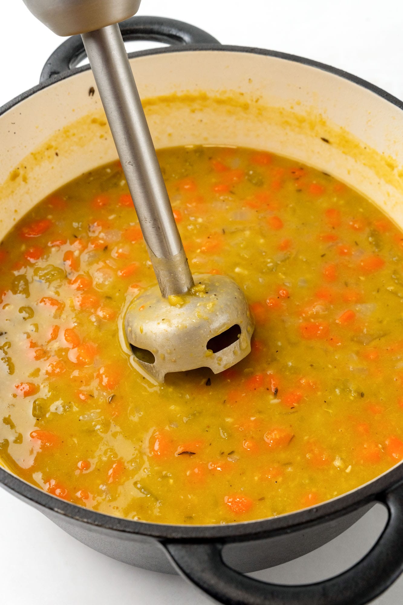 a dutch oven of split pean soup pureed with a hand blender.