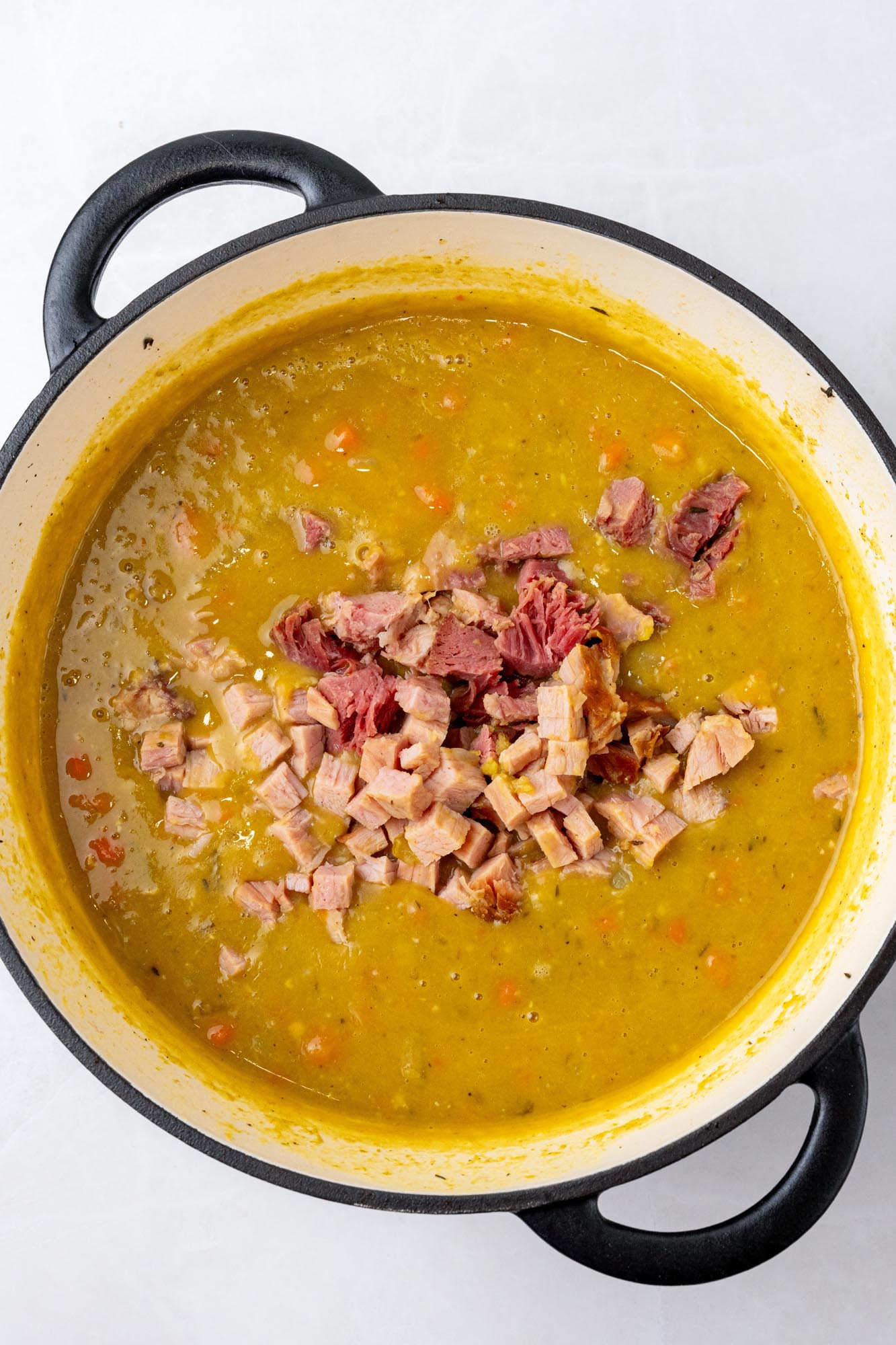 diced ham added to split pea soup in a large pot, viewed from above.
