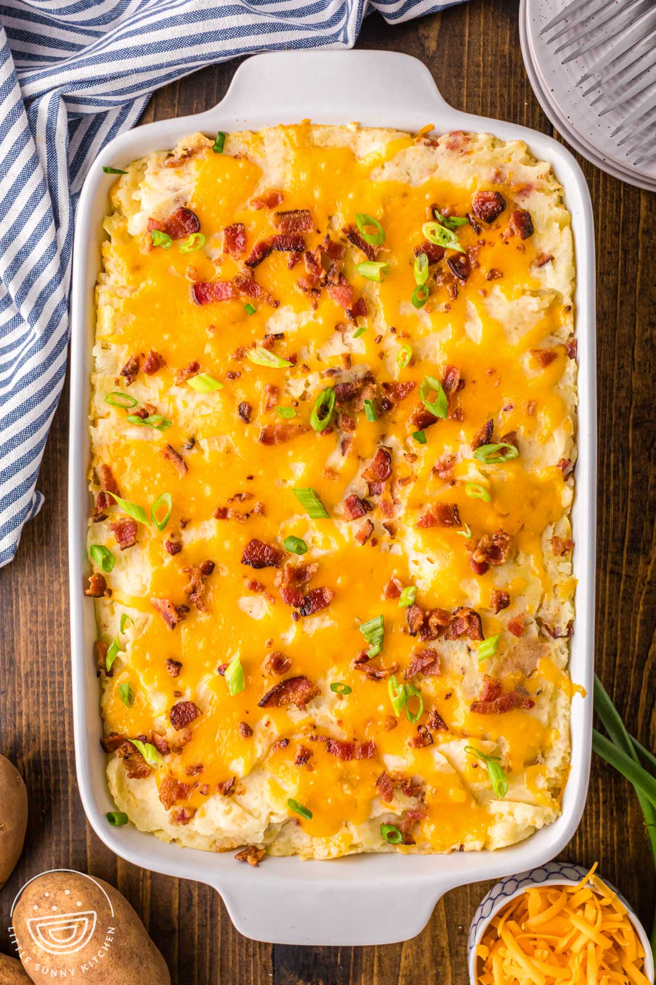 twice baked potato casserole topped with cheese, bacon, and green onions, in a white 9x13-inch baking dish, viewed from above.
