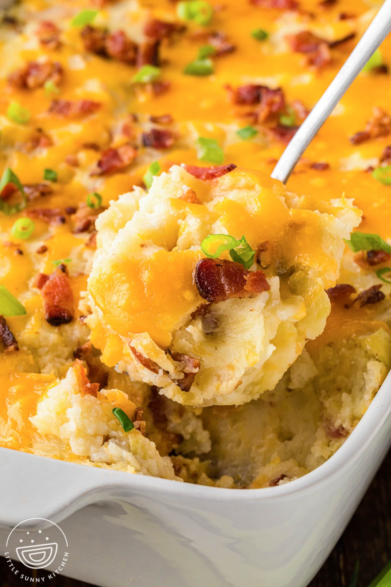 twice baked potato casserole in a baking dish. A serving is lifted out with a spoon. 