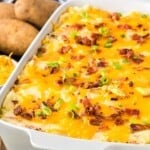 a white casserole dish of cheesy mashed potato casserole with bacon and cheese
