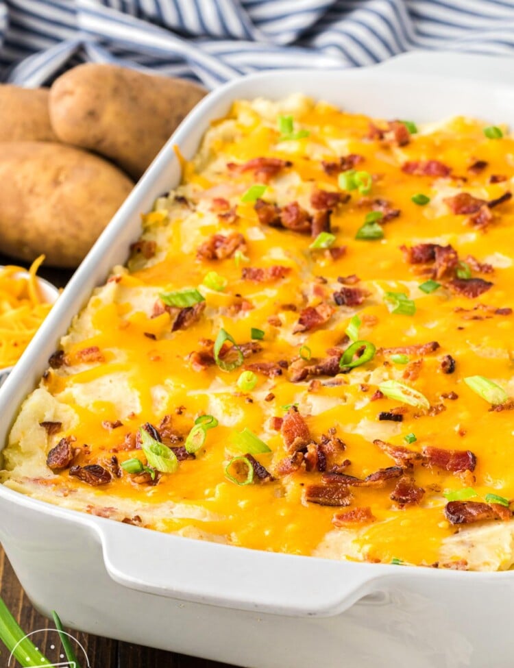 a white casserole dish of cheesy mashed potato casserole with bacon and cheese