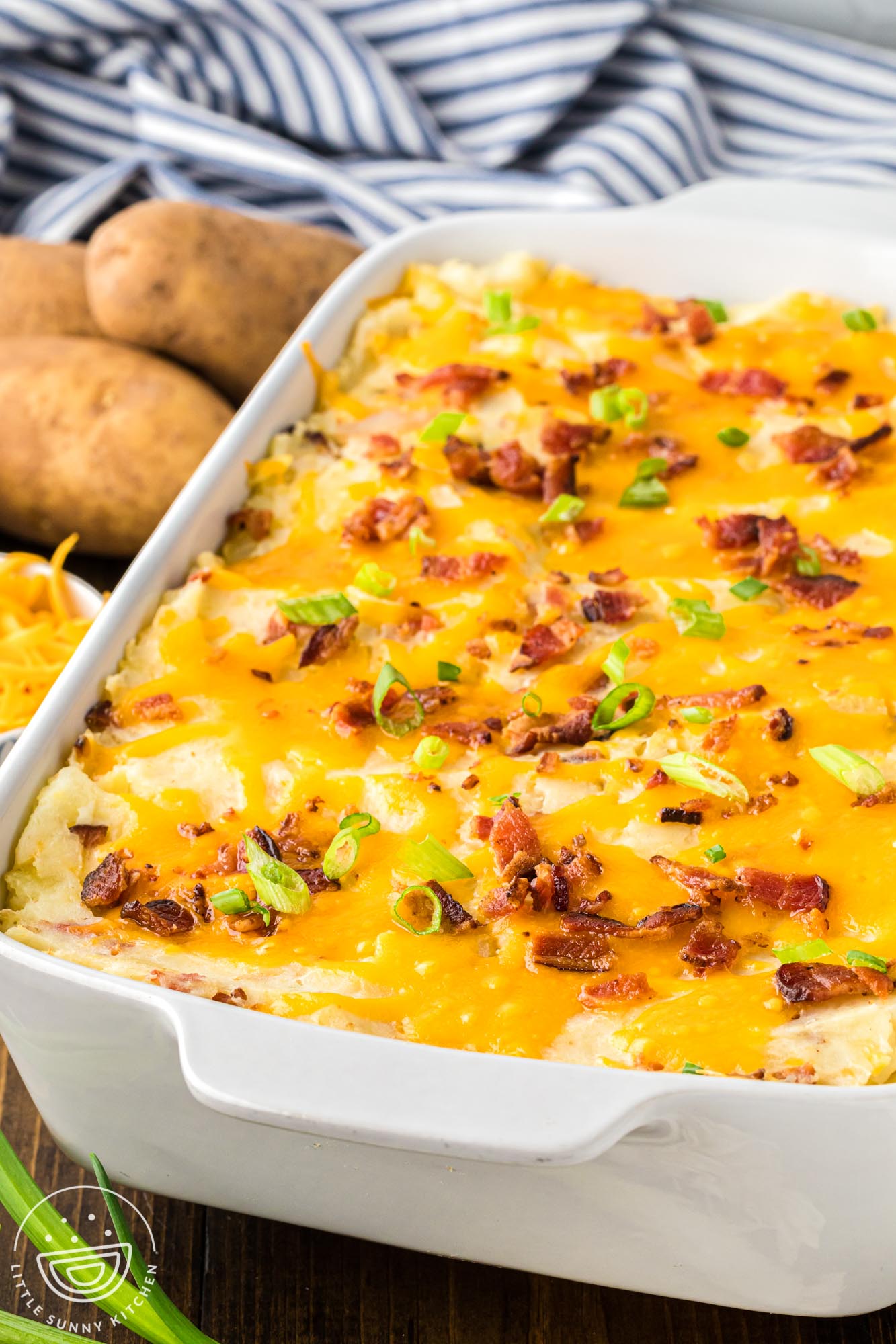 a white casserole dish of cheesy mashed potato casserole with bacon and cheese