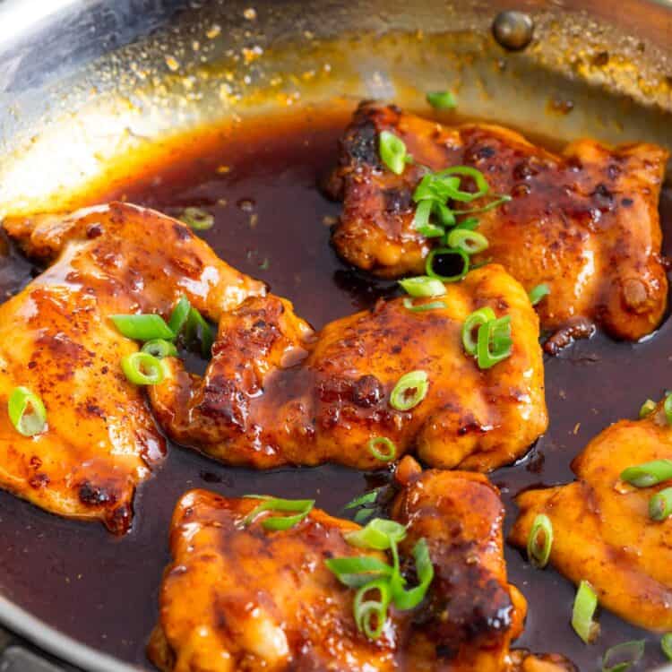 Five boneless chicken thighs in a skillet with apricot glaze.