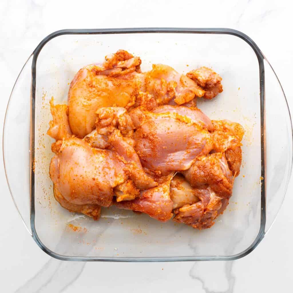 boneless skinless chicken thighs seasoned with paprika, in a glass square dish.