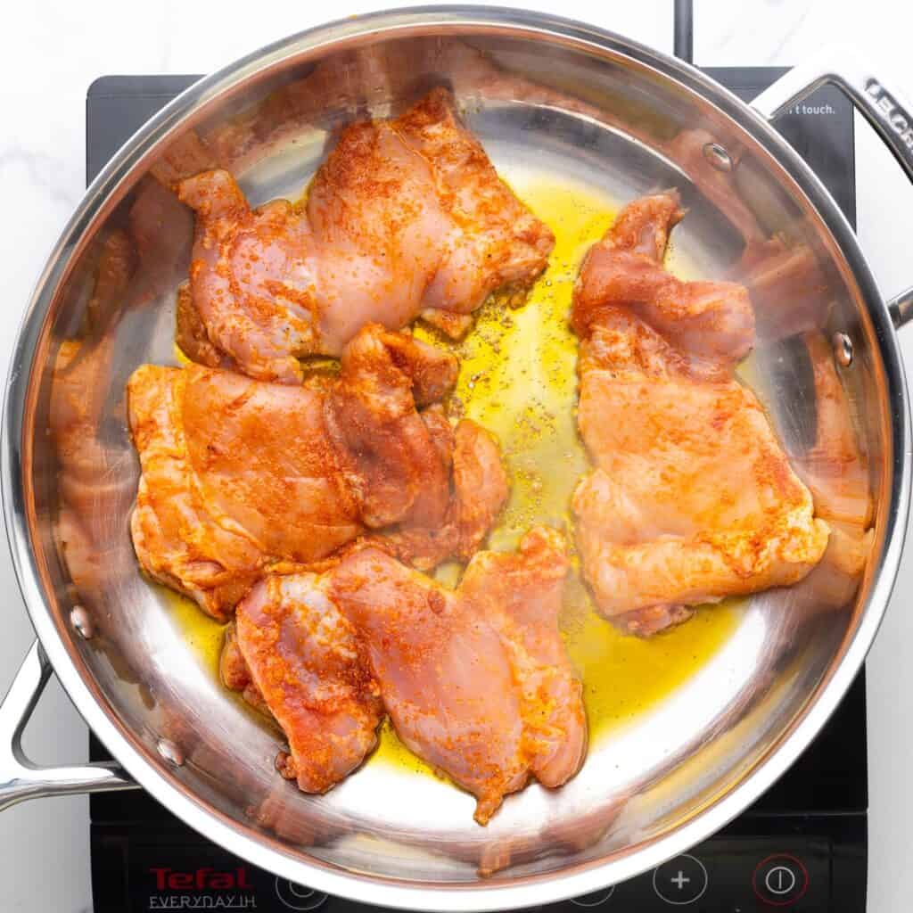 raw, seasoned chicken thighs in a skillet with olive oil