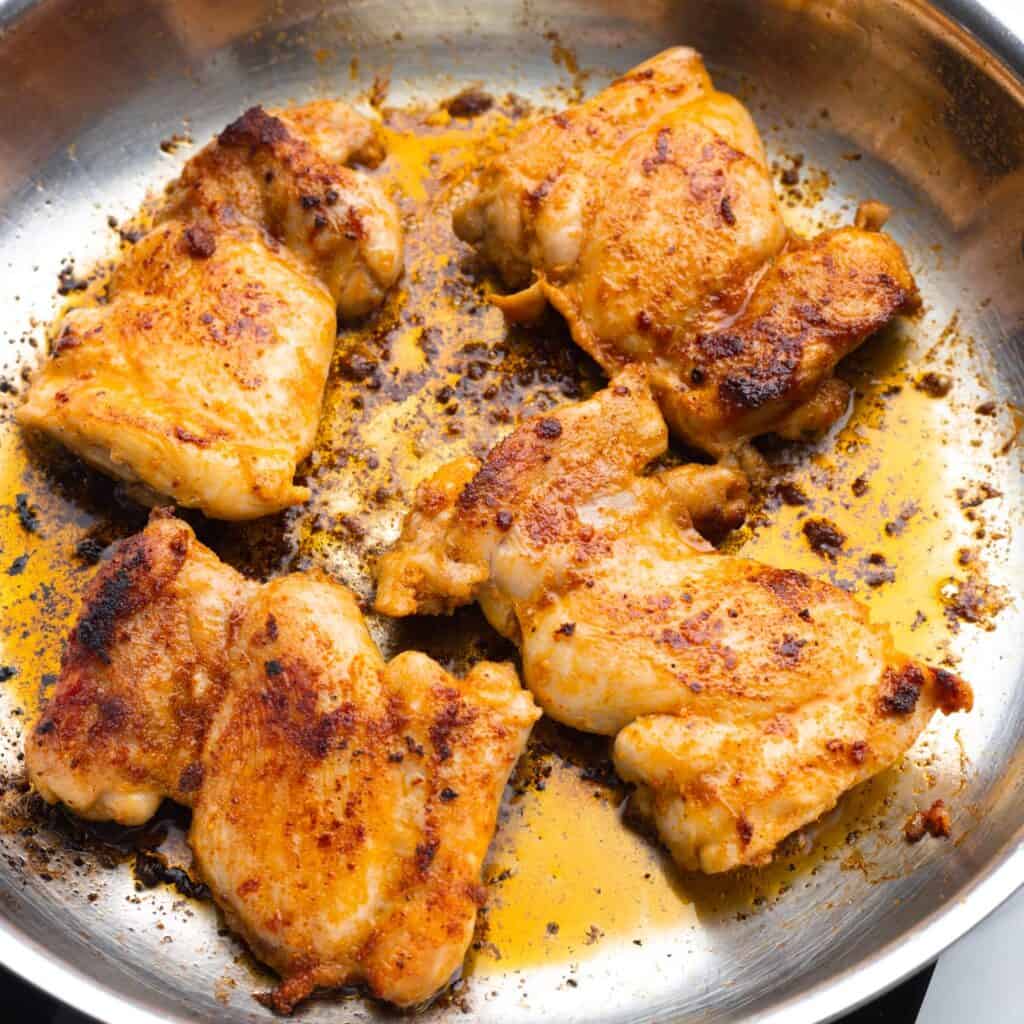 boneless, skinless chicken thighs seared in a stainless steel pan.