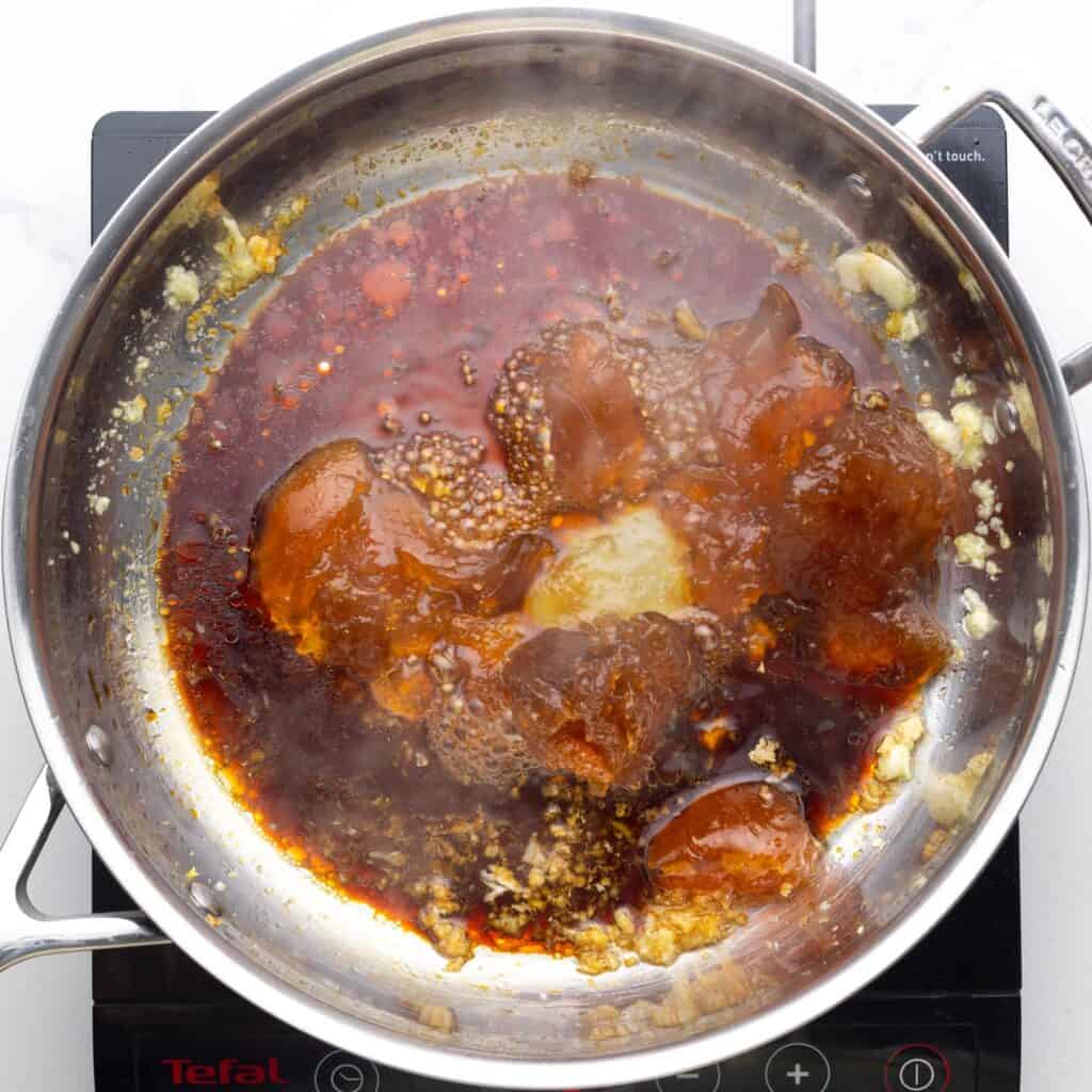 a stainless steel skillet over an electric burner. In the pan is apricot jam, sauteed garlic and seasonings.