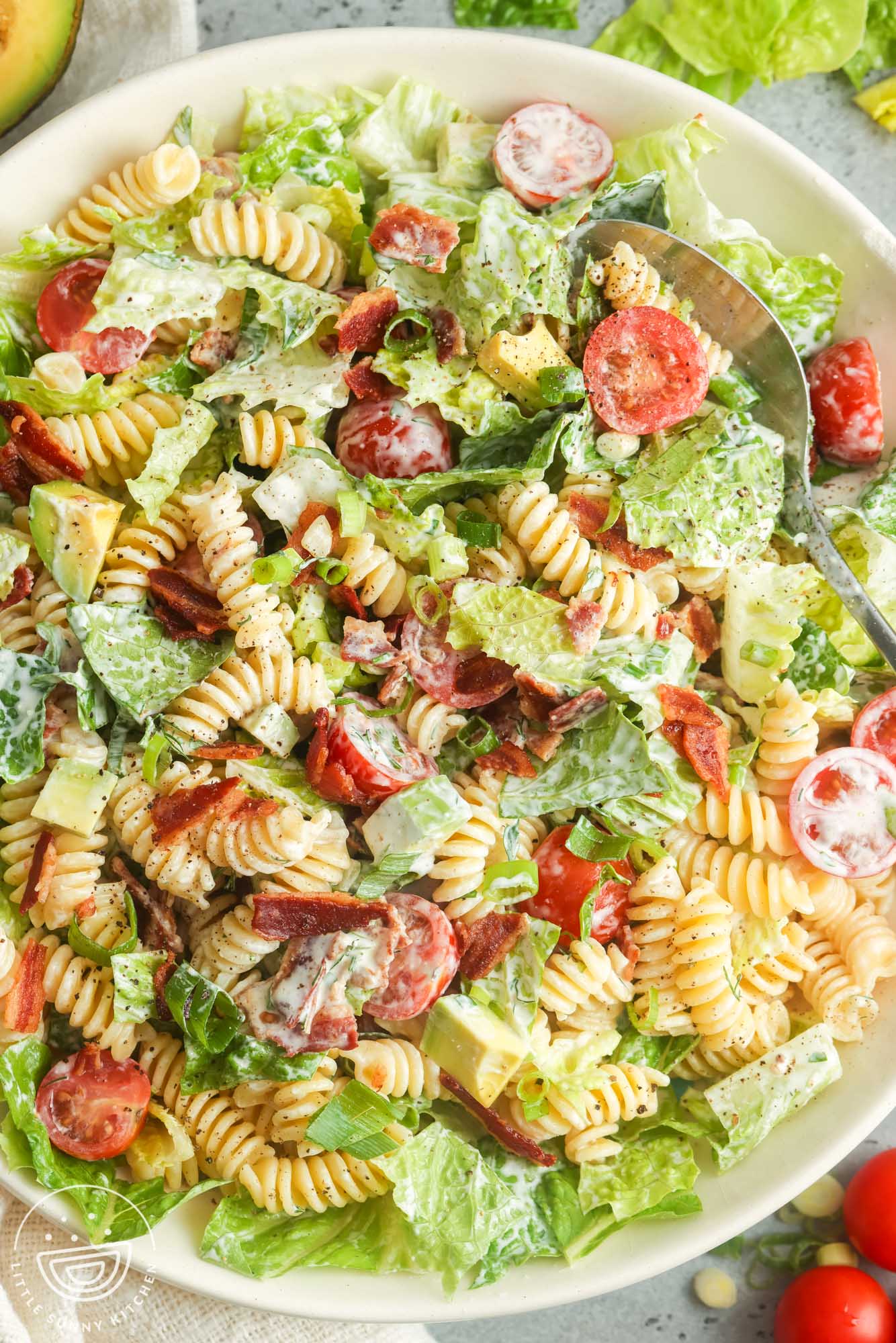 a large white serving bowl of homemade BLT pasta salad with lettuce, cherry tomatoes, and rotini pasta