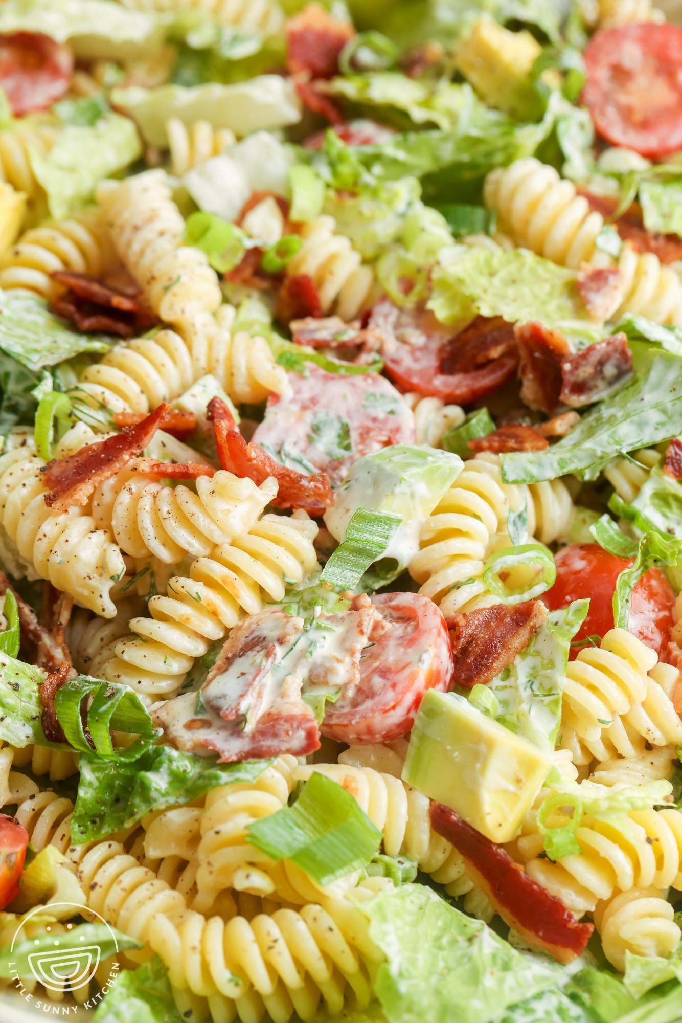 closeup of BLT pasta salad to show the ingredients: diced avocado, pasta, crispy bacon, lettuce, and ranch dressing.