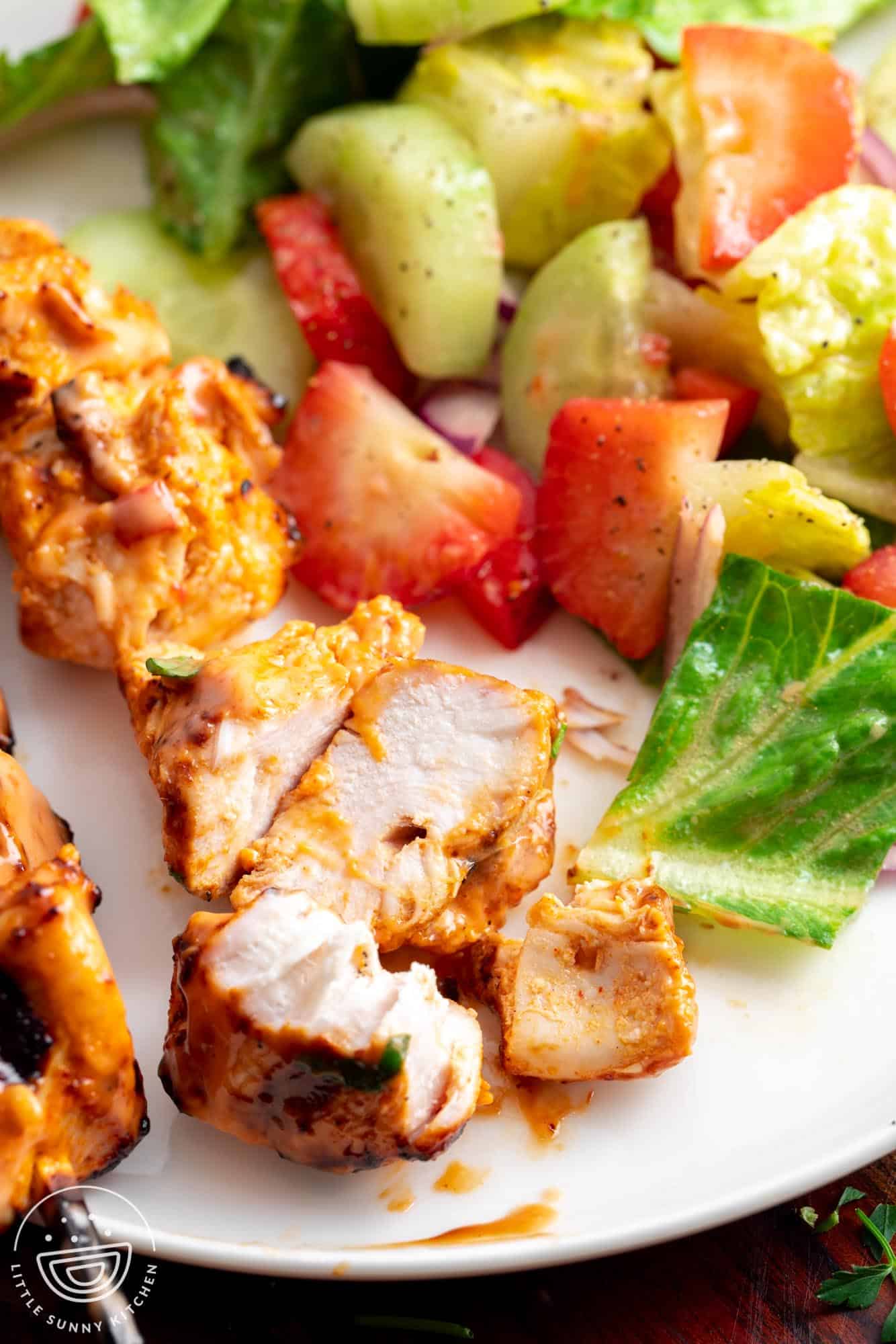 grilled bang bang chicken skewers on a plate with a fresh salad.