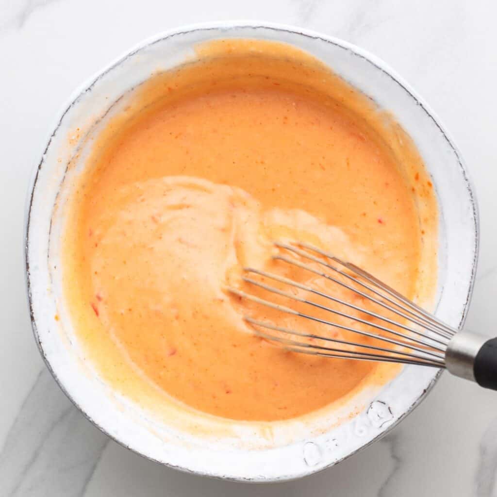 a white ceramic bowl filled with creamy bang bang sauce, stirred with a whisk.