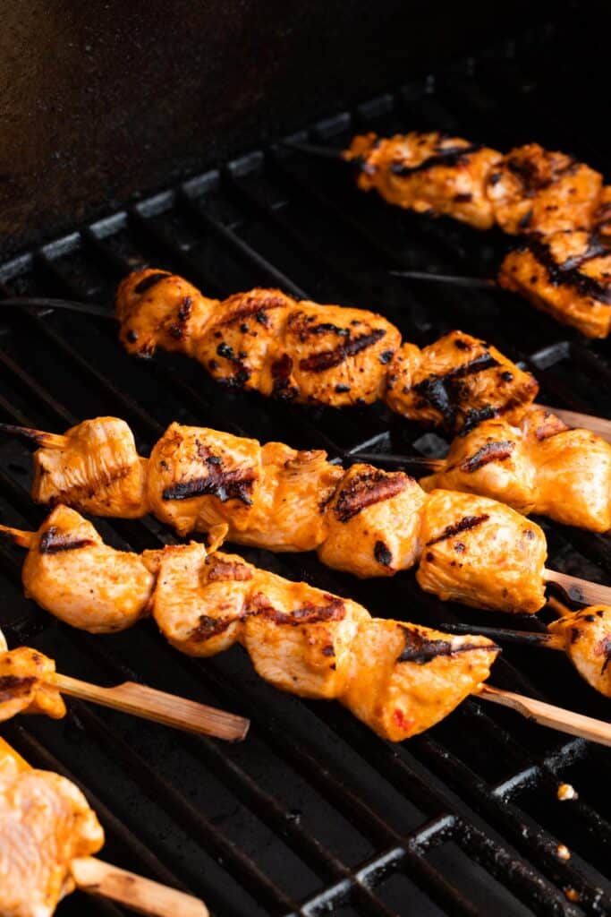 cubes of chicken on wooden skewers, on an outdoor grill.