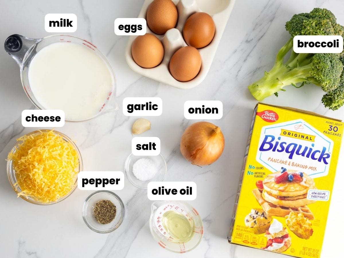 Ingredients for bisquick impossible quiche, including baking mix, cheese, milk, eggs, broccoli, arranged on a marble counter