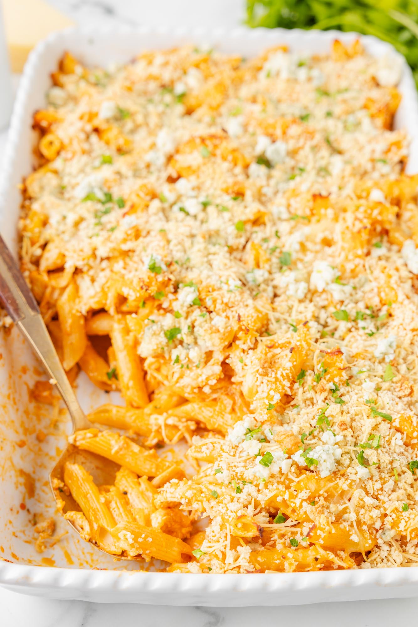 a white rectangular casserole dish holding baked buffalo chicken pasta topped with bread crumbs and cheese.