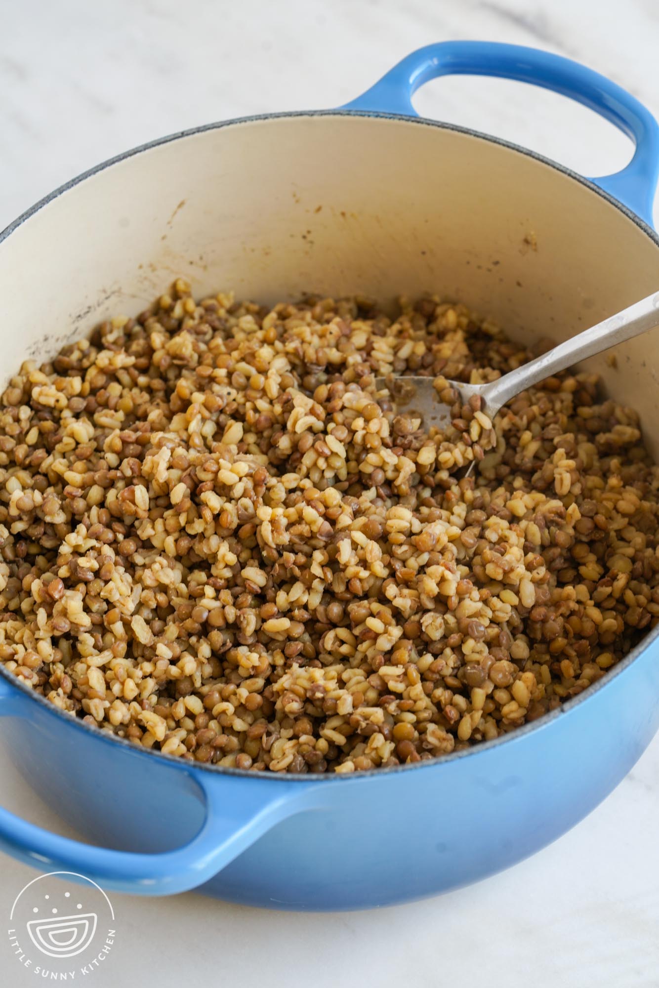 Bulgur and lentils cooked in a large Le Creuset blue dutch oven, with a serving spoon