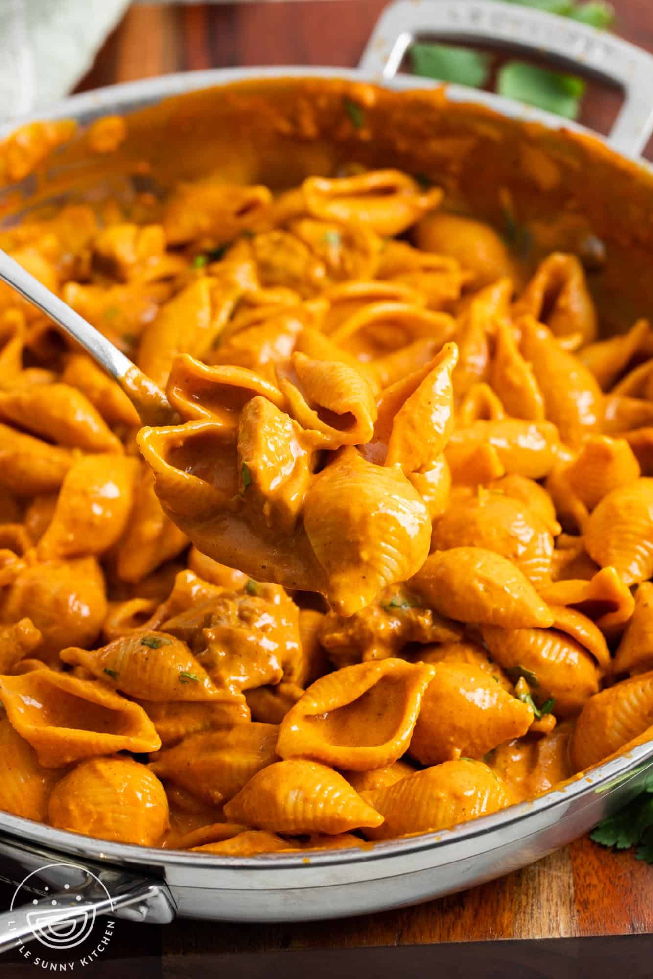 butter chicken pasta in a skillet on the table. A spoon is serving the dish.