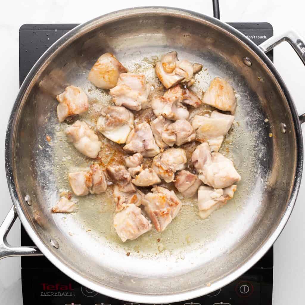 diced chicken thighs cooking in a stainless steel pan with oil.