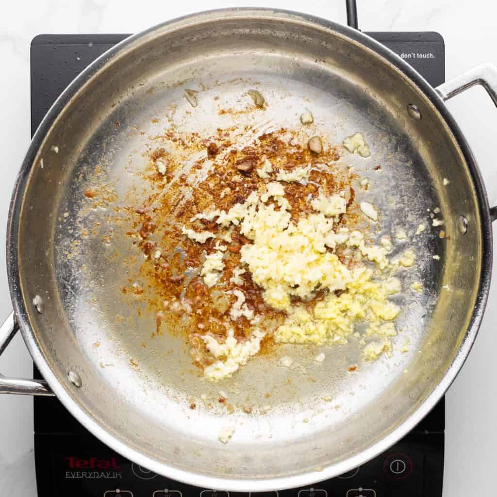 minced garlic added to a skillet with browned bits of chicken.