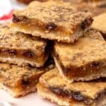 a white ceramic plate holding a pile of butter tart bars with raisins.