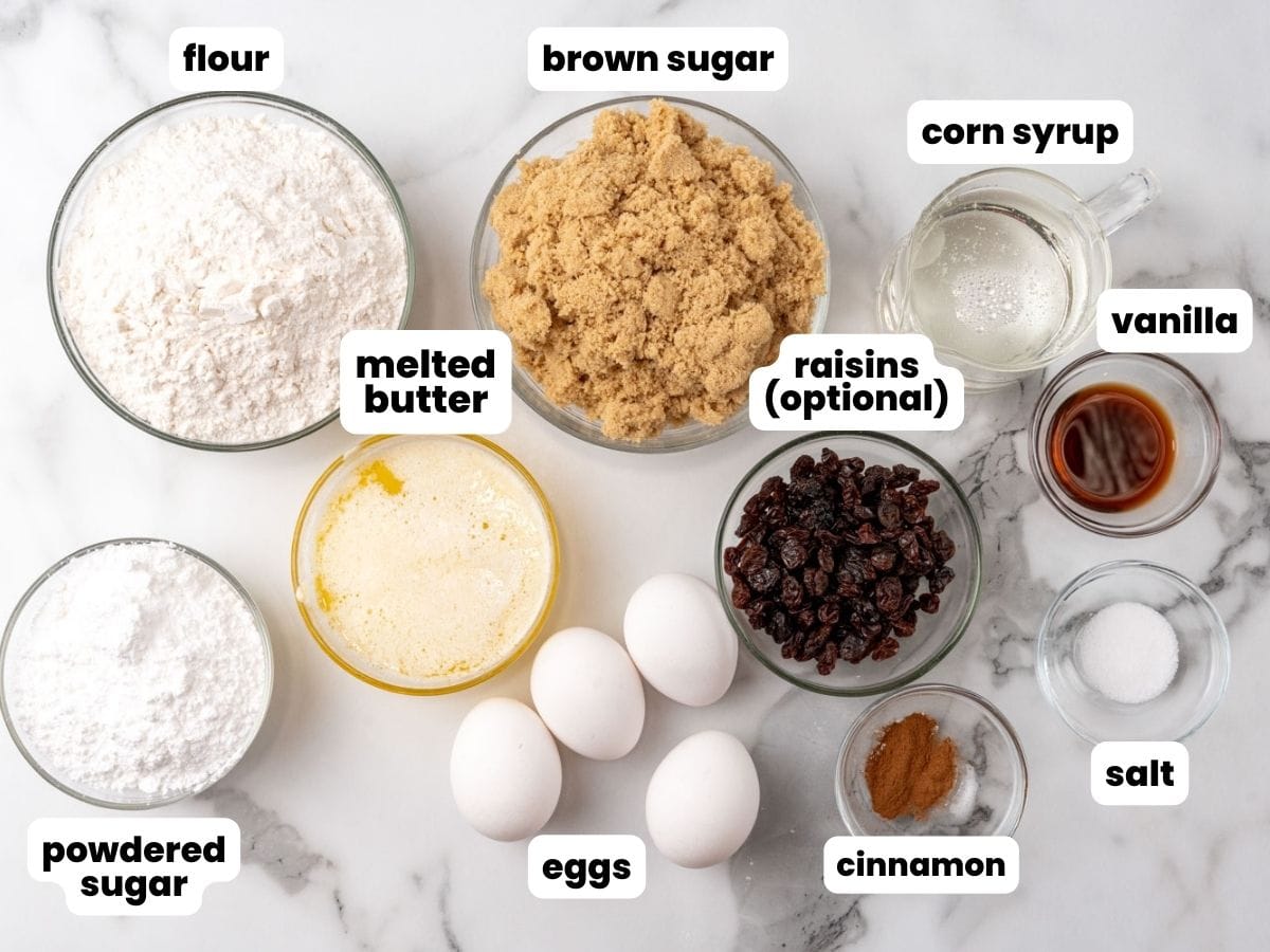 The ingredients needed to make butter tart bars, all measured into small bowls and arranged on a counter. Included are flour, brown sugar, corn syrup ,vanilla, melted butter, raisins, powdered sugar, eggs, cinnamon, and salt.