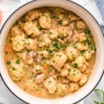 overhead view of a white dutch oven filled with creamy chicken and dumplings with vegetables.