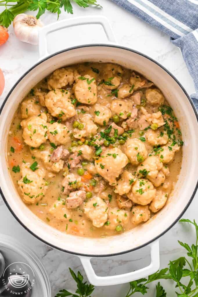 overhead view of a white dutch oven filled with creamy chicken and dumplings with vegetables.