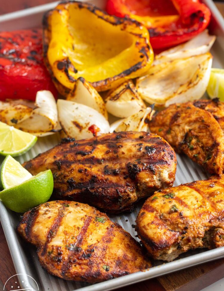 grilled chicken, grilled onion pieces, and grilled yellow and red pepper halves on a sheet tray, garnished with lime wedges.