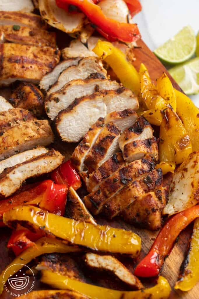 sliced fajita chicken breast with sliced peppers on a wooden cutting board.