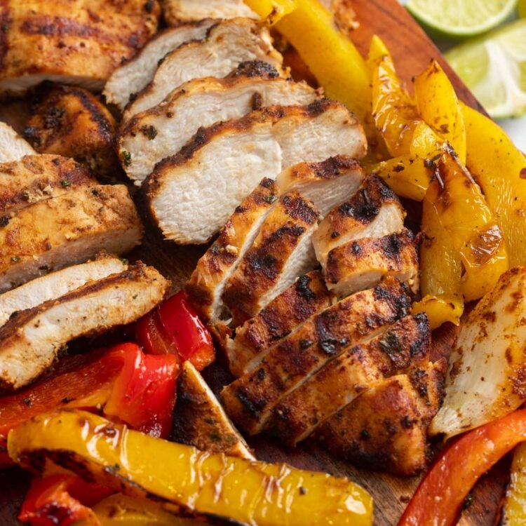 sliced fajita chicken breast with sliced peppers on a wooden cutting board.