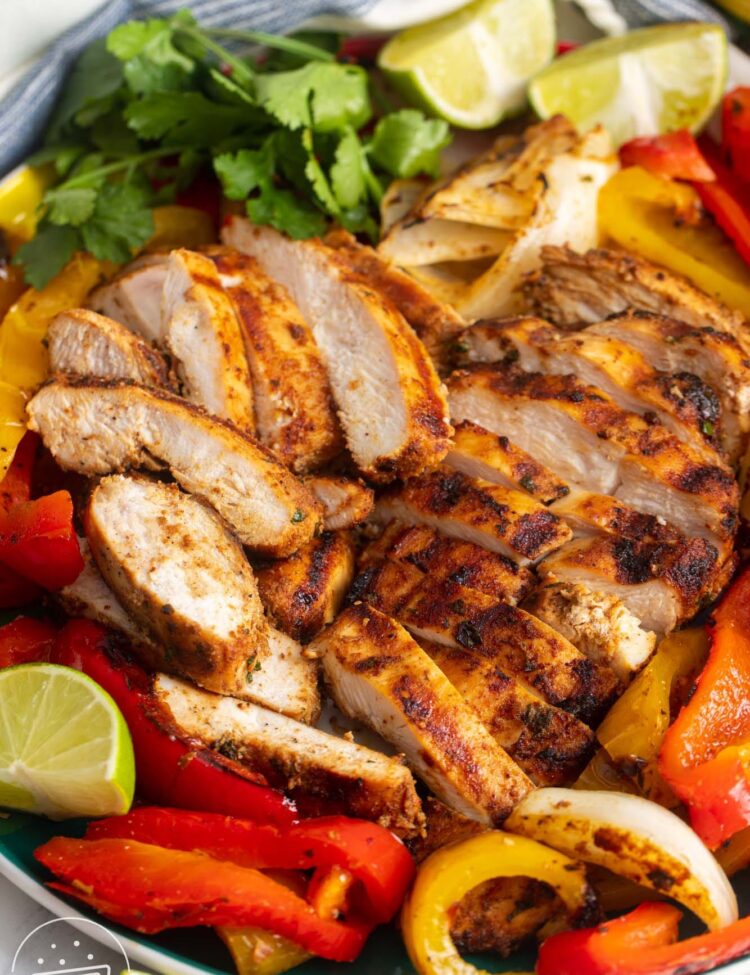 grilled chicken fajitas on a plate, garnished with fresh cilantro and lime wedges.
