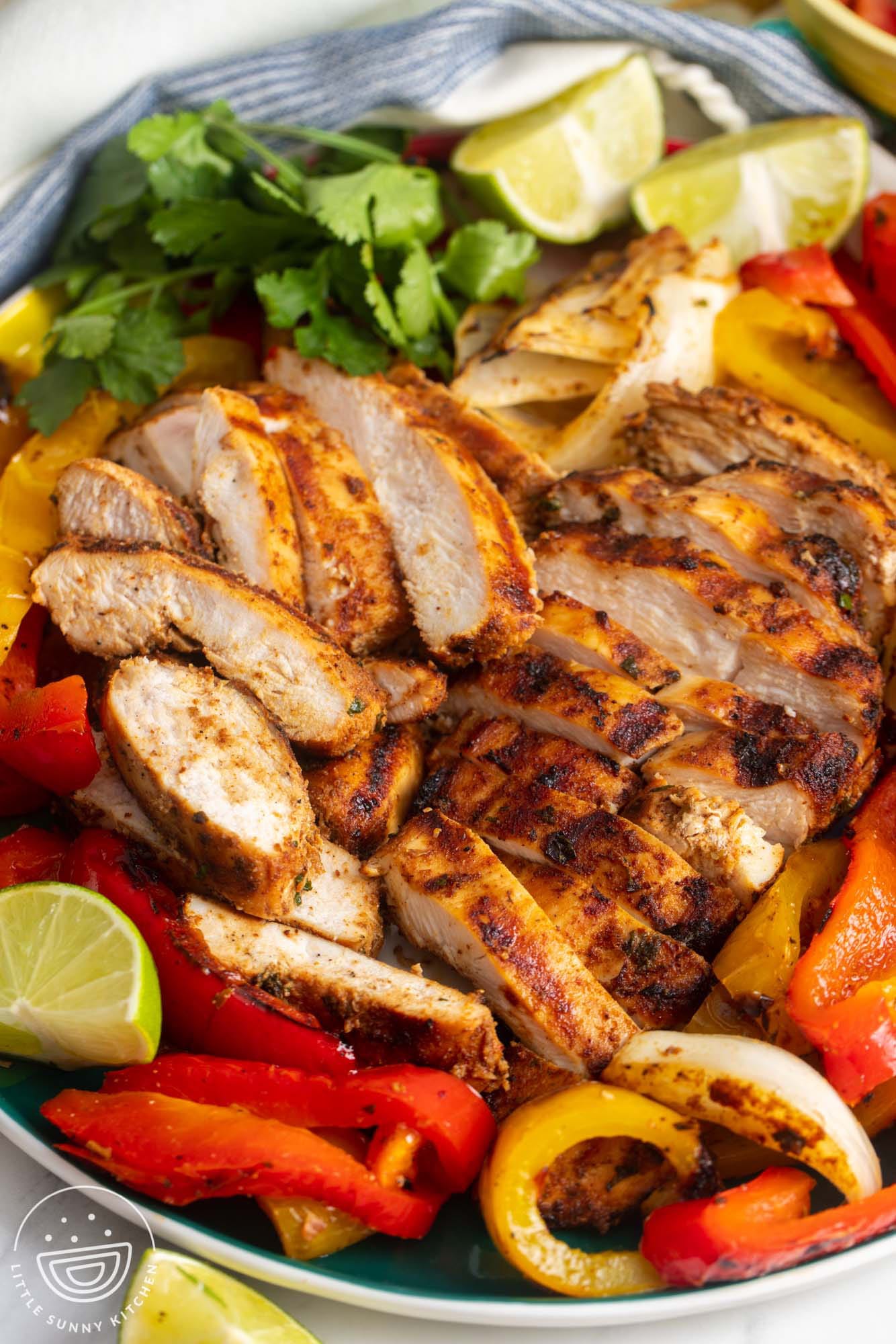 grilled chicken fajitas on a plate, garnished with fresh cilantro and lime wedges.