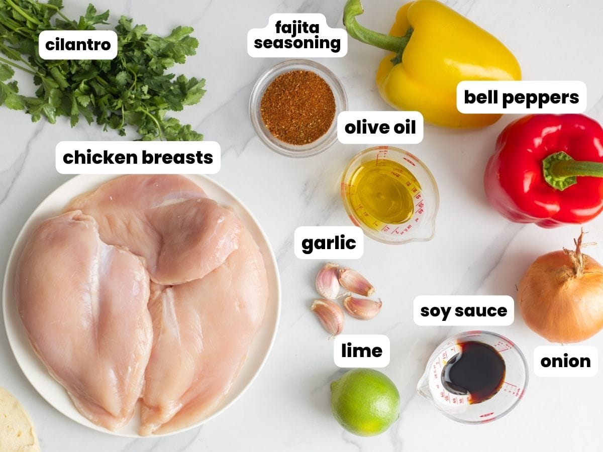 The ingredients needed to make chicken fajitas, including chicken breasts, bell peppers, onion, garlic, lime, seasoning.
