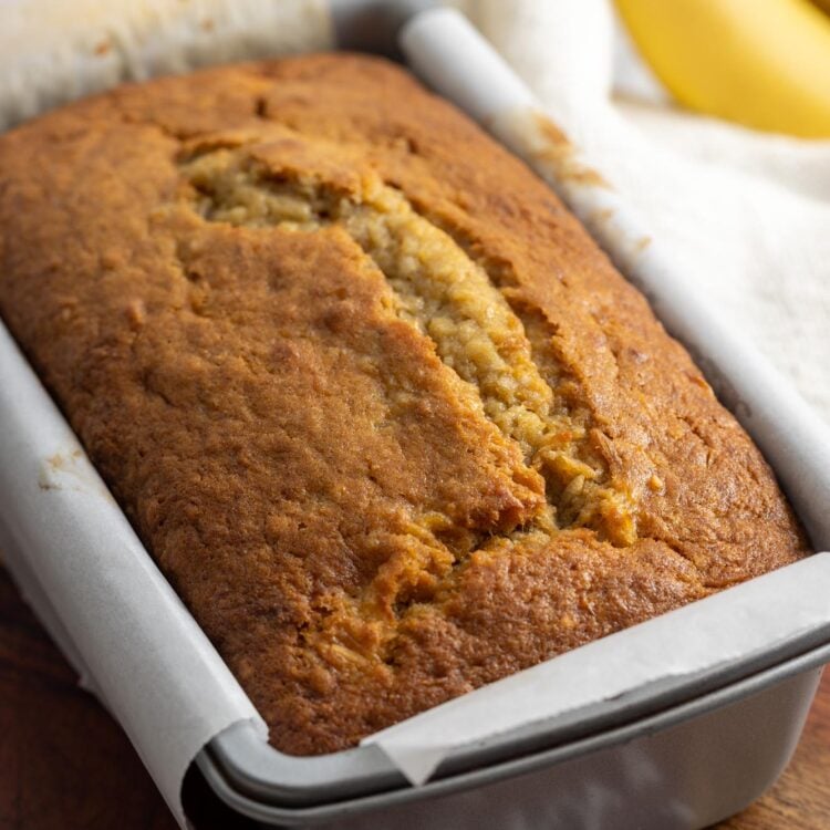 Baked banana bread in a loaf pan lined with parchment paper.