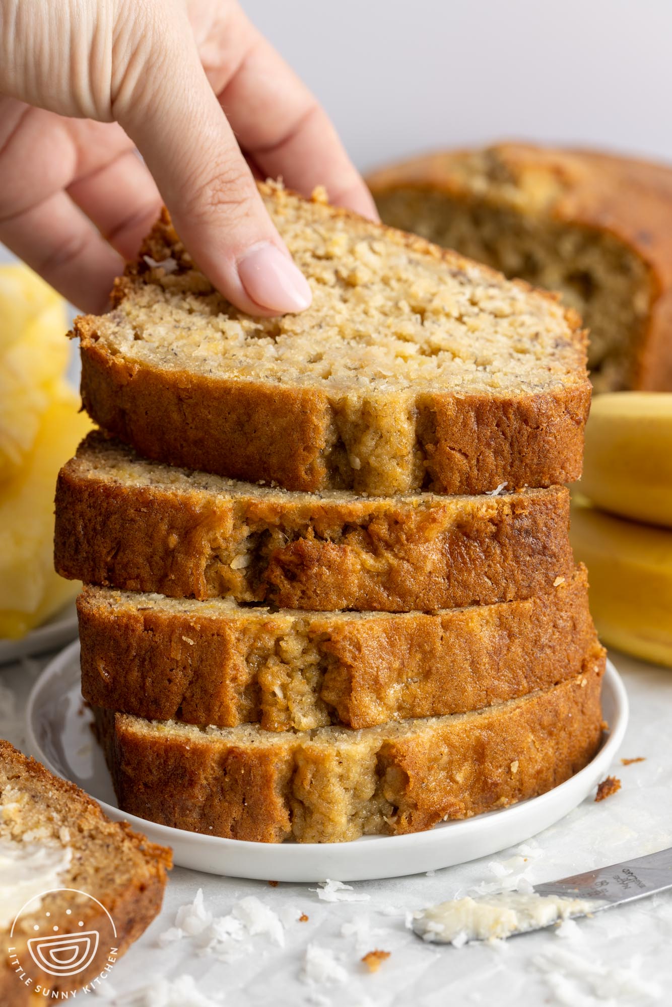 a stack of thick slices of banana bread on a plate. A hand is picking a slice from the pile.