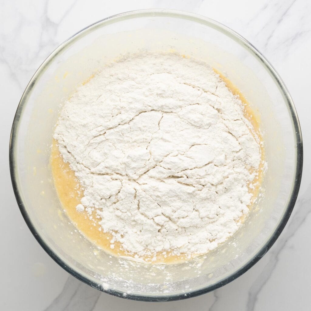 dry ingredients added to wet ingredients for banana bread in a large glass mixing bowl.