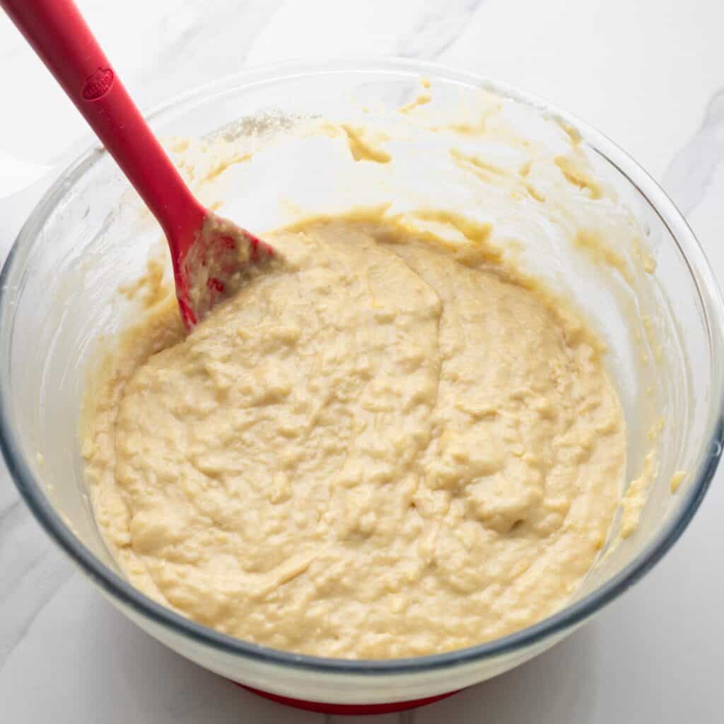 banana bread batter stirred in a glass bowl with a red spoon.