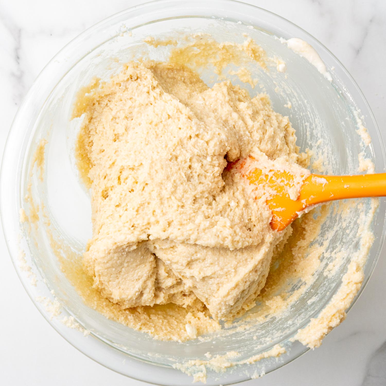 cottage cheese cookie dough stirred together in a glass mixing bowl with an orange spoon.