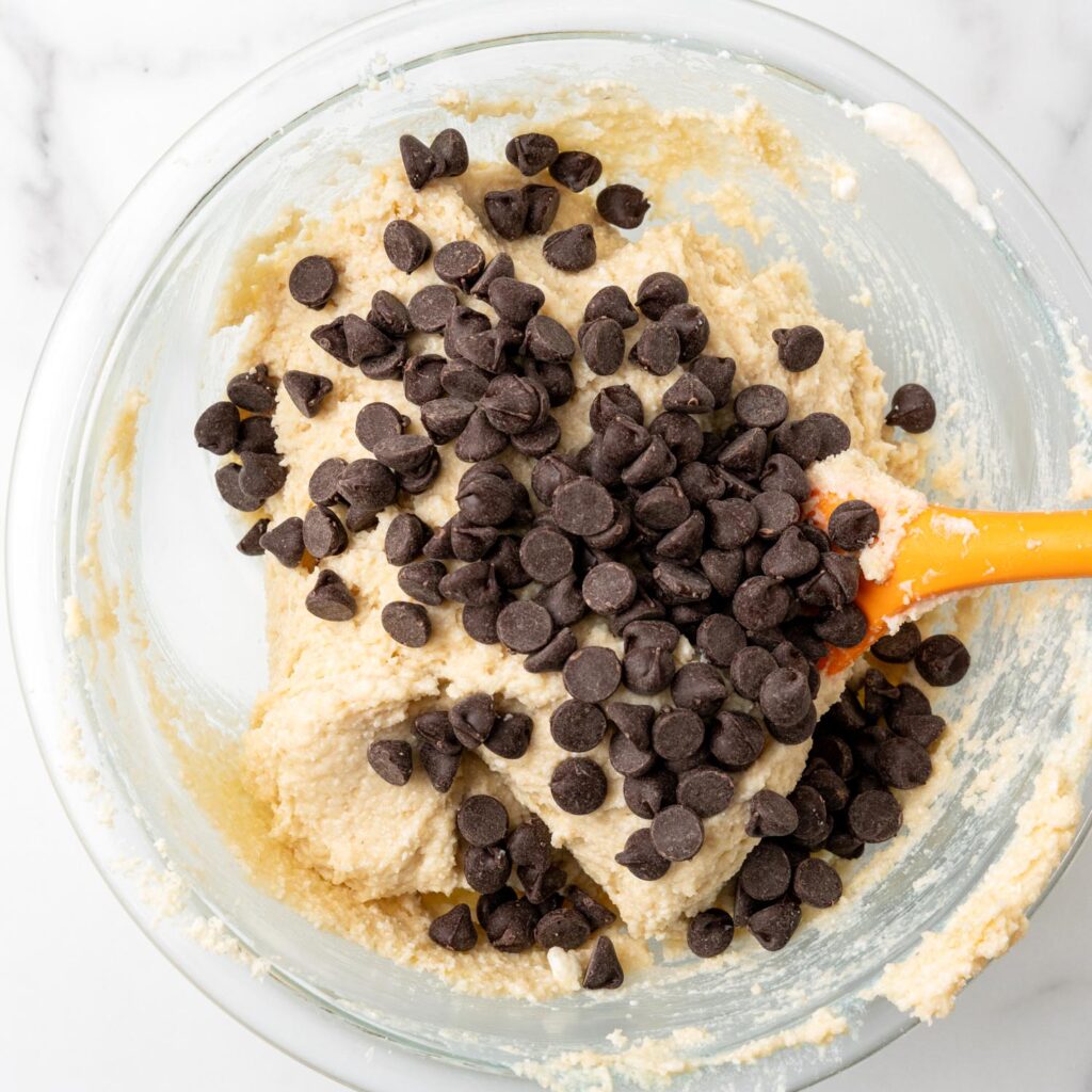 chocolate chips added to smooth cottage cheese cookie dough in a glass bowl.