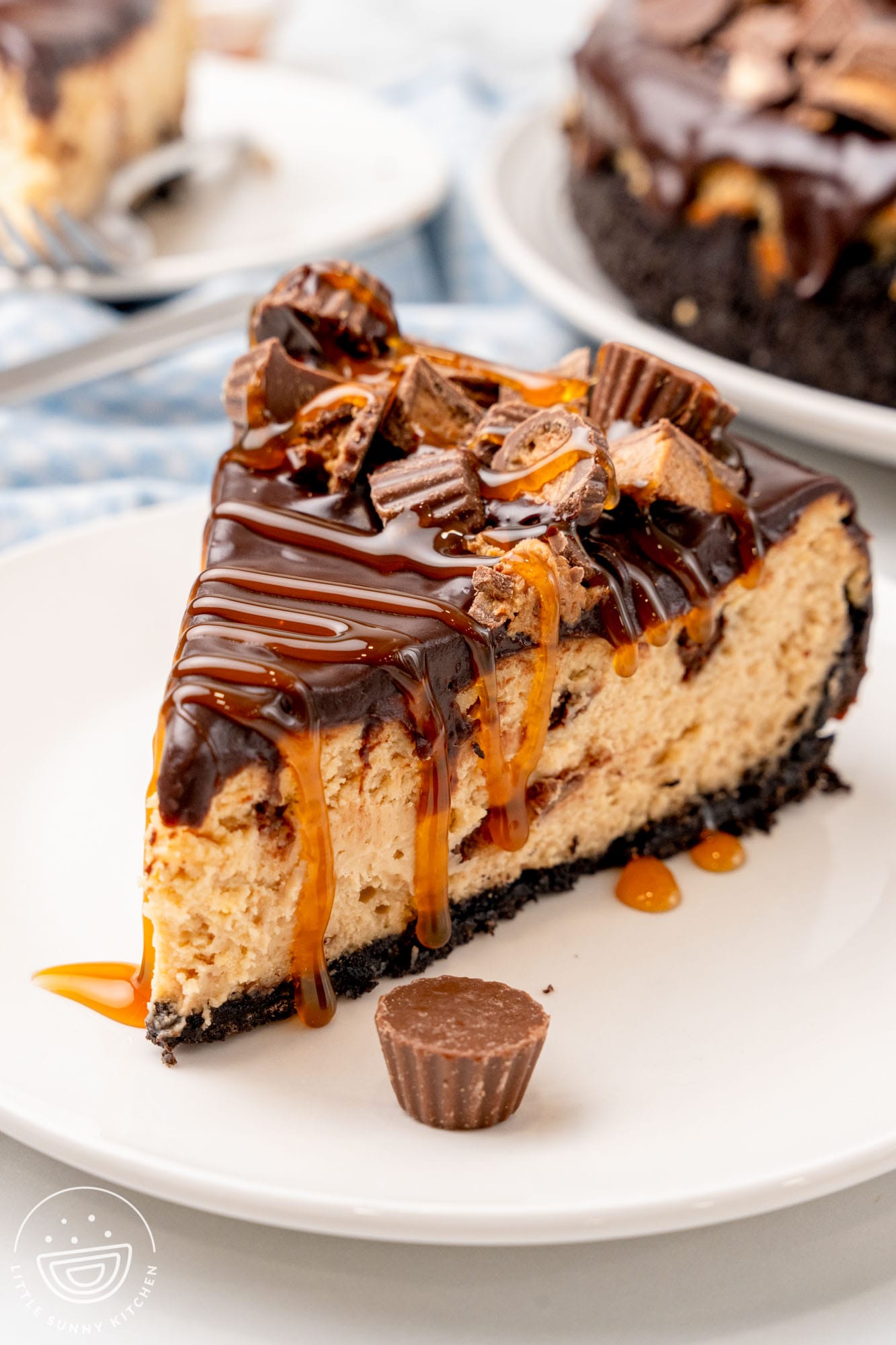 A small white plate holding a slice of homemade Reese's caramel cheesecake, drizzled with caramel sauce and topped with peanut butter cups.