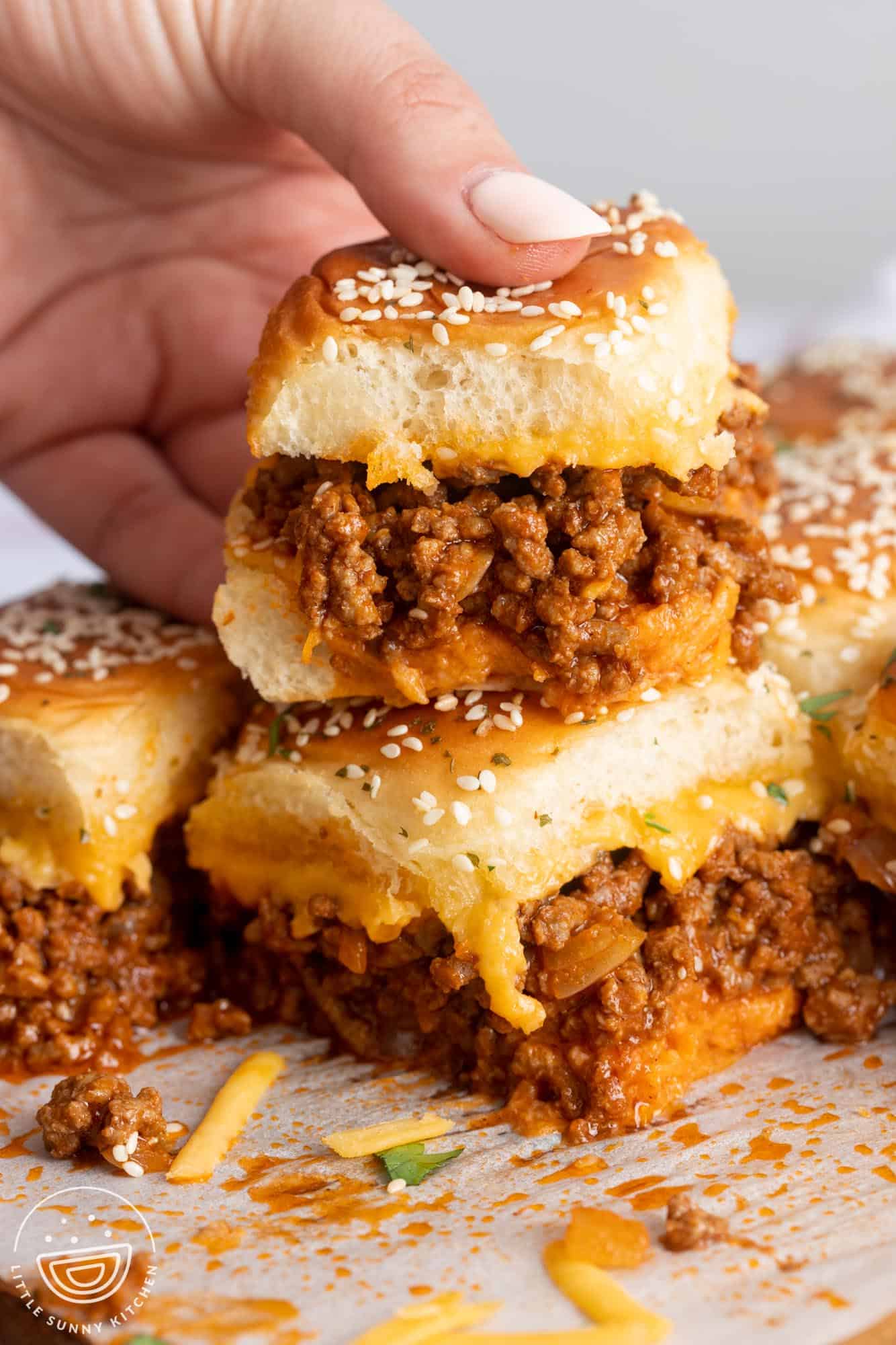 a hand holding a cheesy, freshly baked sloppy joe slider.