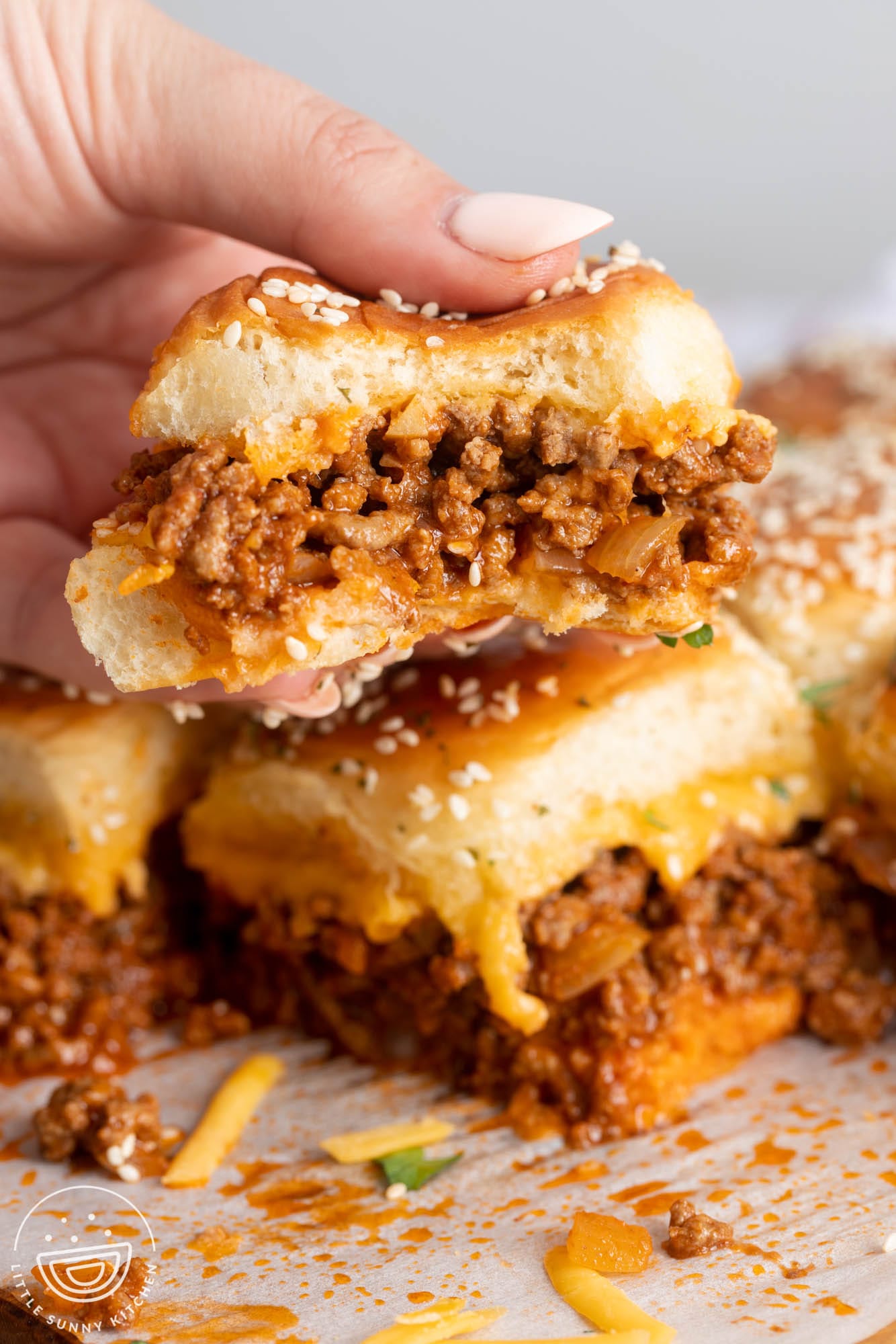 A hand picking up a freshly baked Sloppy Joe slider from a full tray.