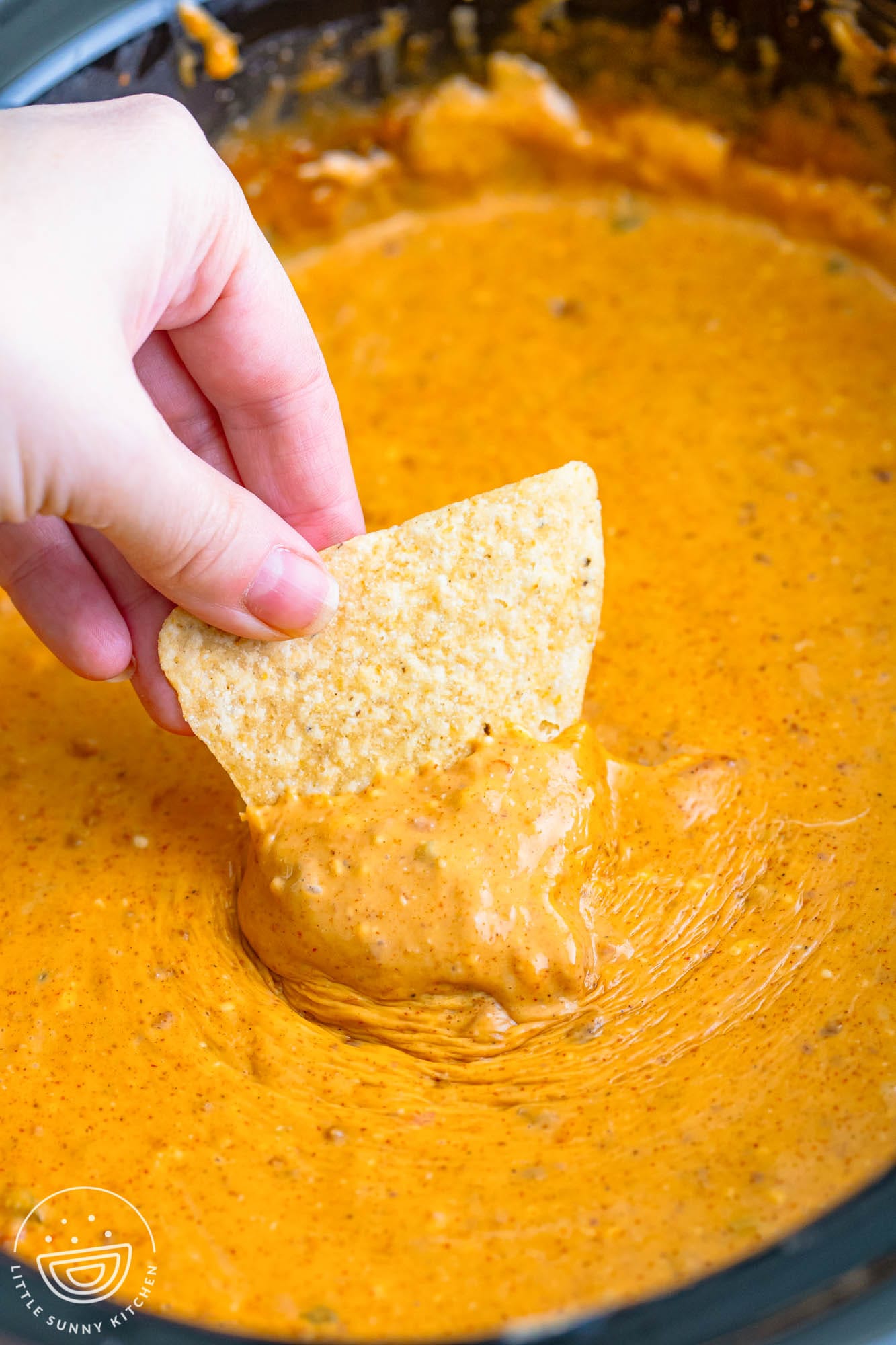a hand dipping a tortilla chip into a crock pot filled with queso dip.