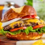 a cheeseburger on a dark bun with sliced onion, sliced tomatoes, and green leaf lettuce.