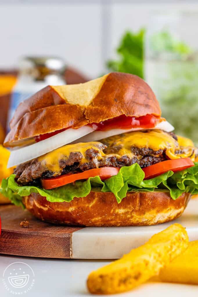 a cheeseburger on a dark bun with sliced onion, sliced tomatoes, and green leaf lettuce.