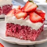 a square slices of strawberry cake with fluffy frosting and sliced strawberries on top