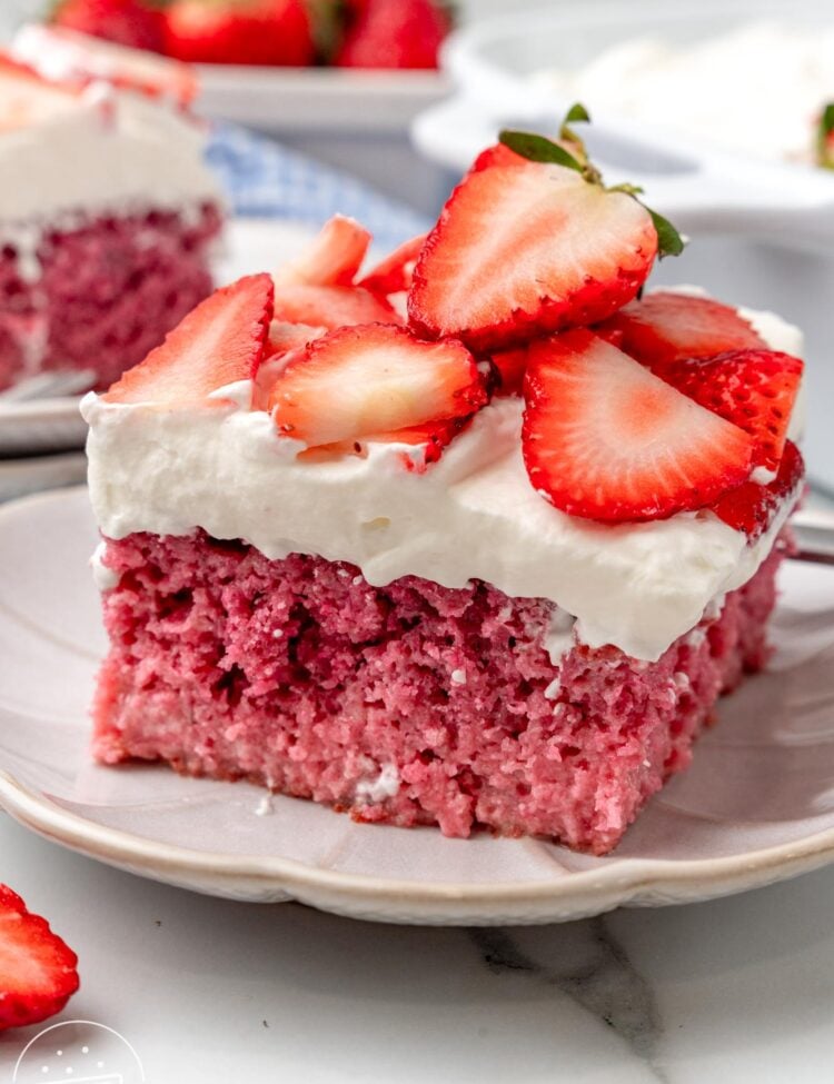 a square slices of strawberry cake with fluffy frosting and sliced strawberries on top