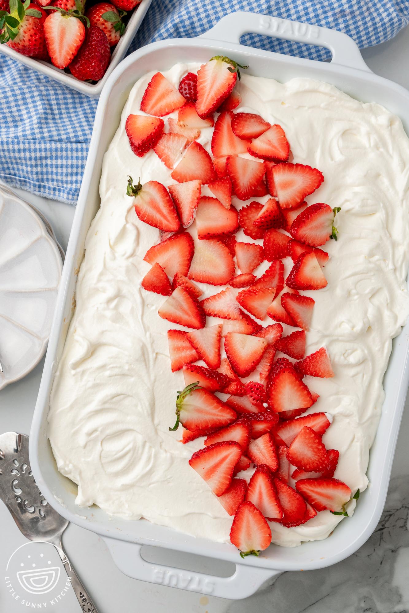 strawberry tres leches cake baked in a white 9x13 dish, topped with whipped cream and strawberry slices. 