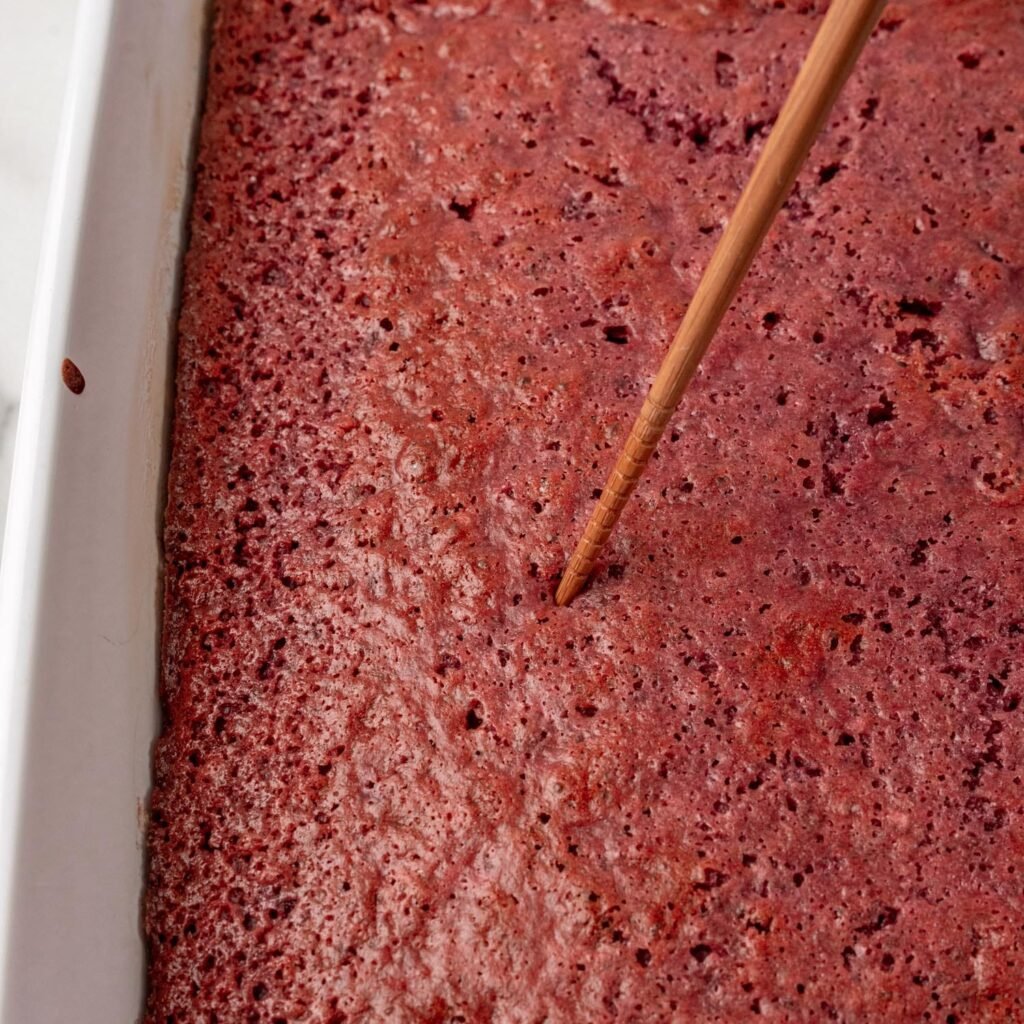 a chopstick poking holes into a baked strawberry cake. 